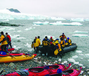 Tourists in boat in Antarctica with kayaks on rocky shore
