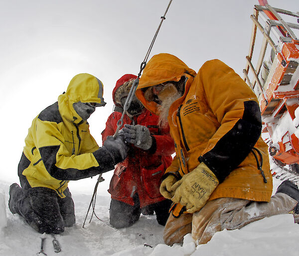 Three expeditioners outdoors gathered around a cable