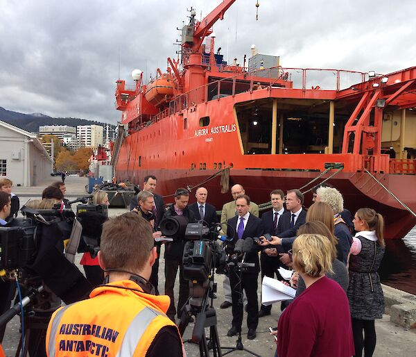 Environment Minister Greg Hunt surrounded by media in front of the orange icebreaker ship Aurora Australis on Hobart's waterfront.