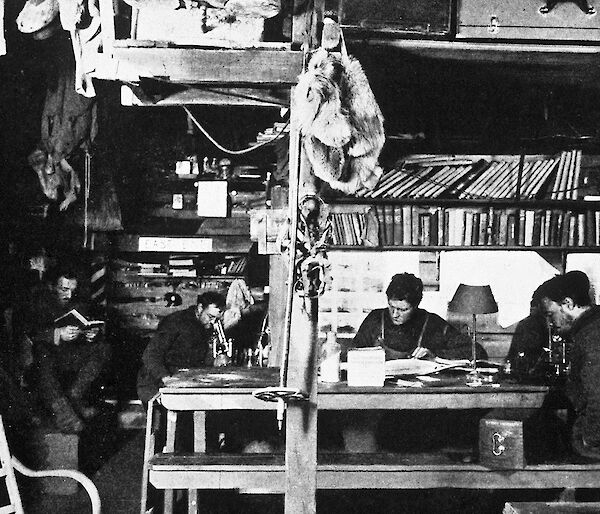 A winter afternoon in the living hut at Commonwealth Bay. (L-R) Dr Xavier Mertz (reading), Archie McLean, Cecil Madigan, and John Hunter.