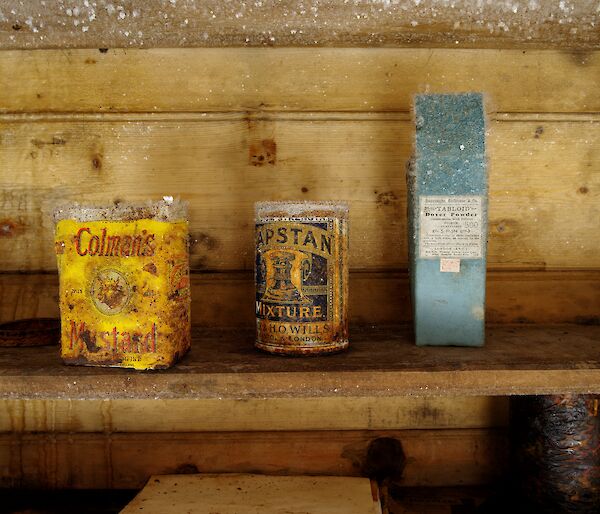 Old tin of mustard and two other original packets on an icy wooden shelf