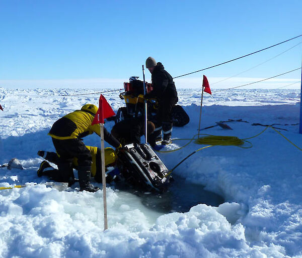 Scientists lower scientific equipment into a hole in the ice.