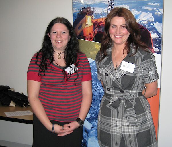 Two female teachers stand in front of a poster of the research vessel, Aurora Australis.