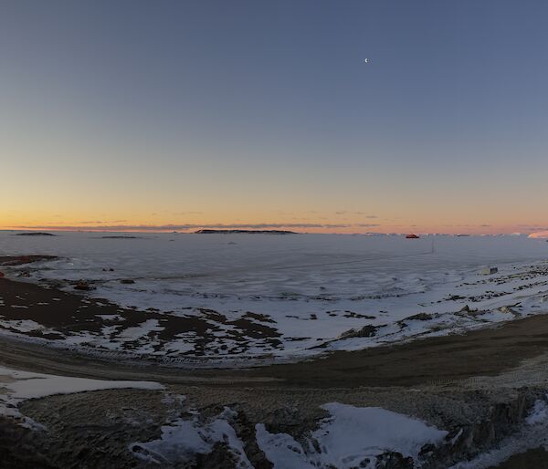 A panoramic view taken from Davis station of the sun low over Prydz Bay, with the Aurora Australis and a hagglund in view.