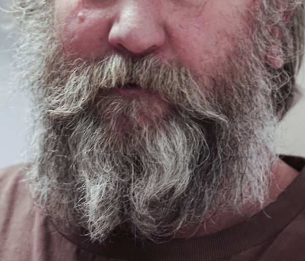 Photo of a man’s face form the nose down with a white and grey-haired beard.