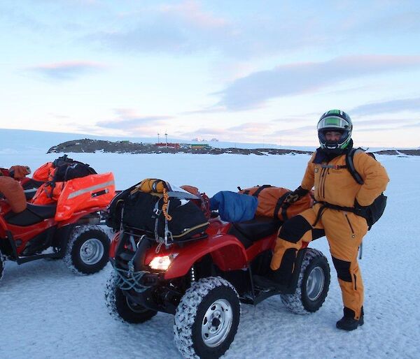 an expeditioner standing beside her quad bike with Mawson Station in the background
