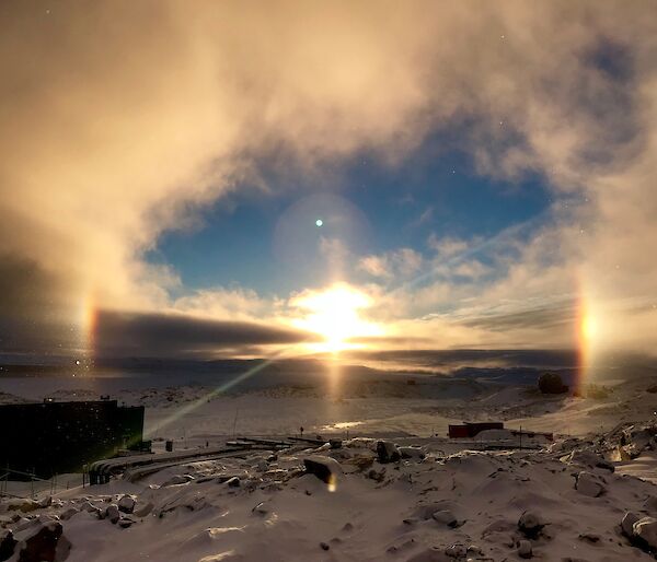 View across Newcomb Bay from Casey Station looking towards the sun coming up over the horizen with a halo created around the sun and sun dogs (mock suns) either side of the sun on the horizen