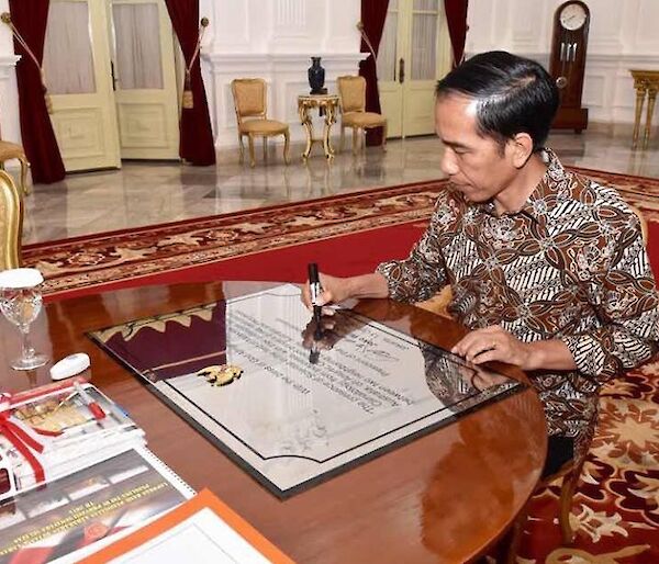 The Indonesian President siting at a desk signing a plaque