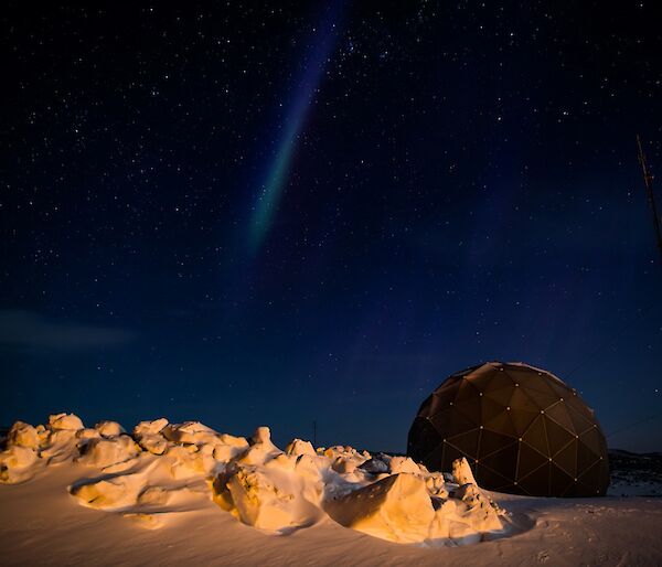 Moonlit snow under a starry sky with a weak aurora by the satellite dome.