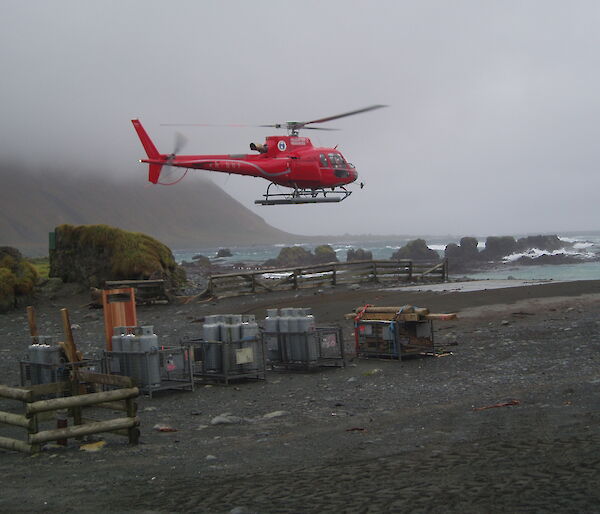 A helicopter lands amongst cargo on a dark and pebble covered beach