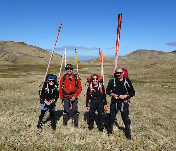 Tasmanian Parks Ranger team standing in a green and brown meadow with orange markers strapped to their backpacks.