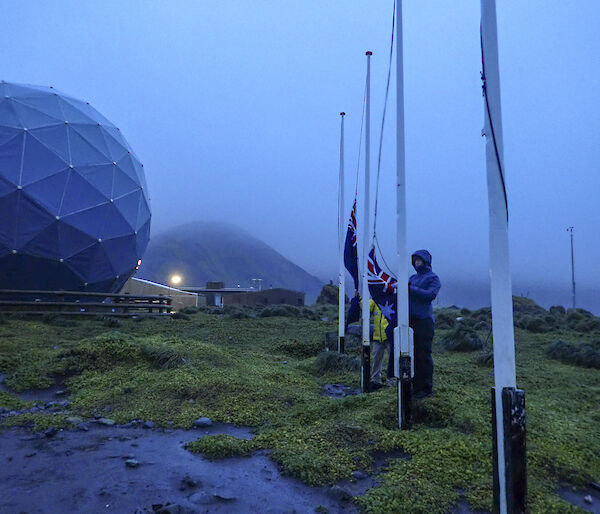 Two raincoat wearing epeditioners raise the NZ and Australian flags at dawn (0632) on the isthmus Macquarie Island