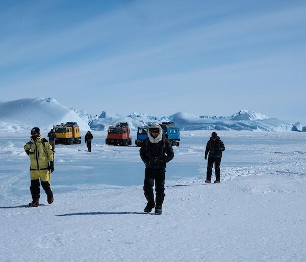 A group of people walk away from the vehicles near some icebergs