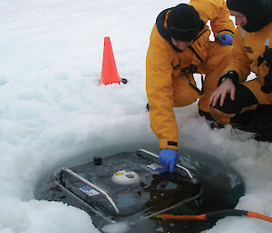 Two scientists peer at the underwater sea ice measuring vehicle through a hole in the ice.