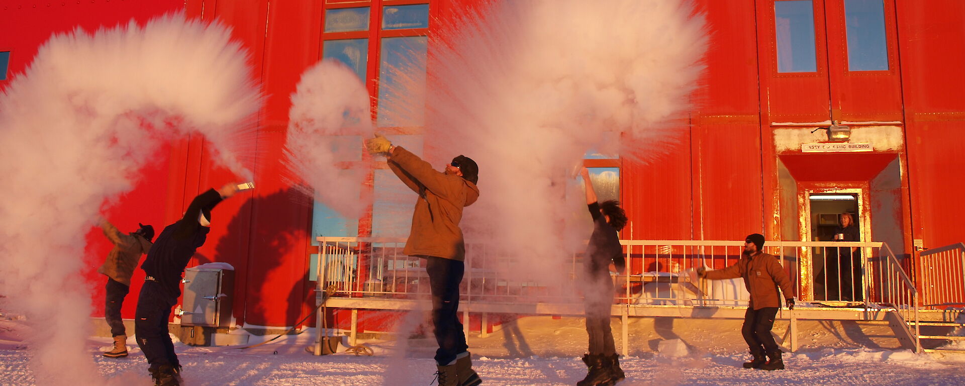 A team of expeditioners throwing boiling water from jugs into the cold air