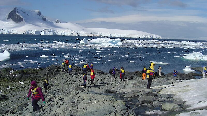 People walking around on the rocky shore with icy mountain in the background