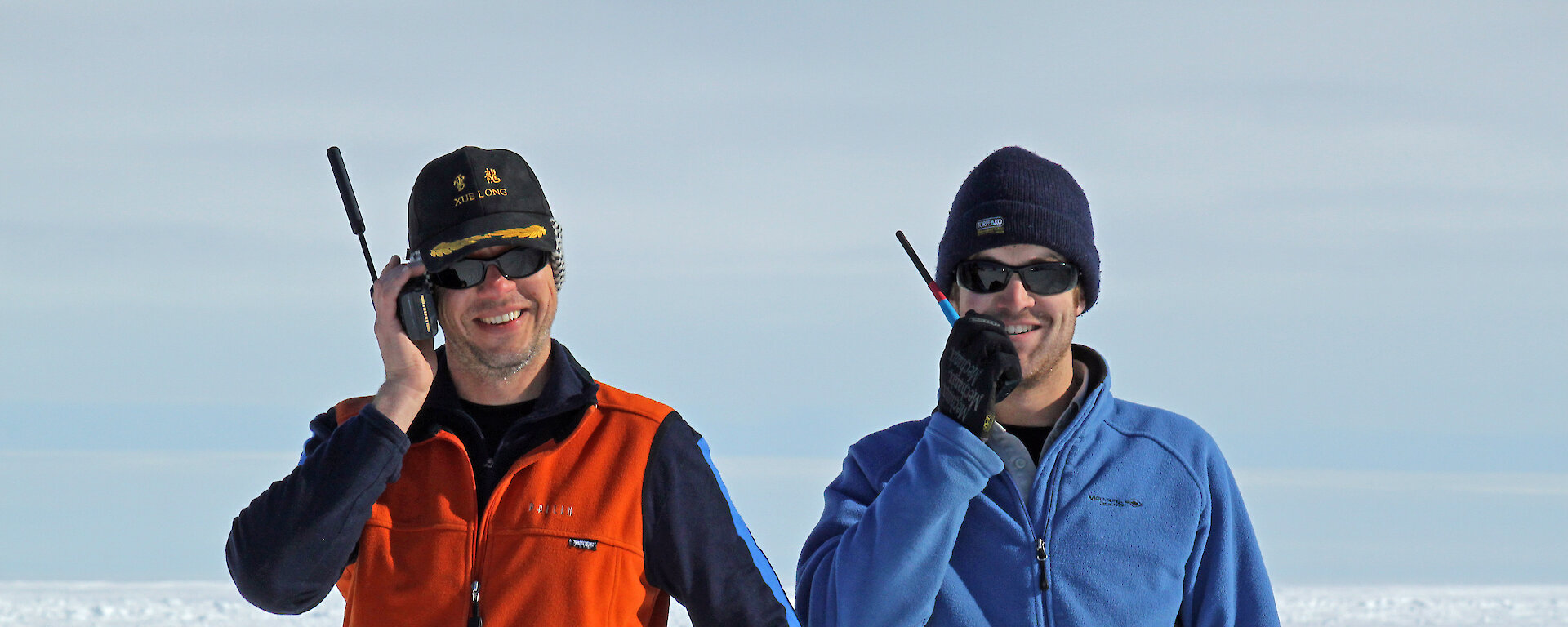 Two expeditioners talk into hand-held radios.