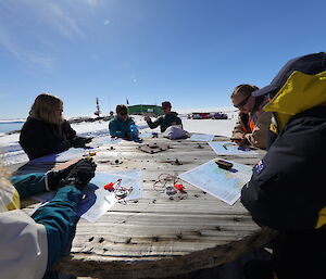 A group of expeditioners gather around an outdoor table to look at maps.