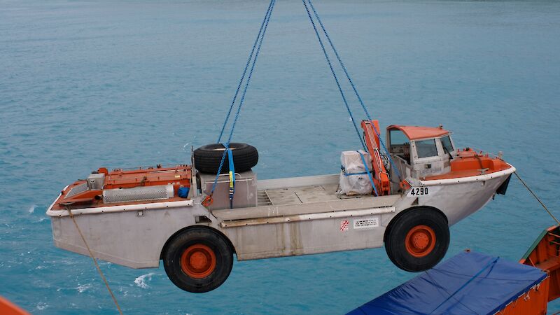 The LARC is lifted in a sling from a crane off the ship onto land.