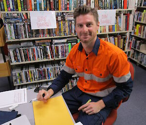 Postmaster wearing high-vis gear ssitting at computer in library