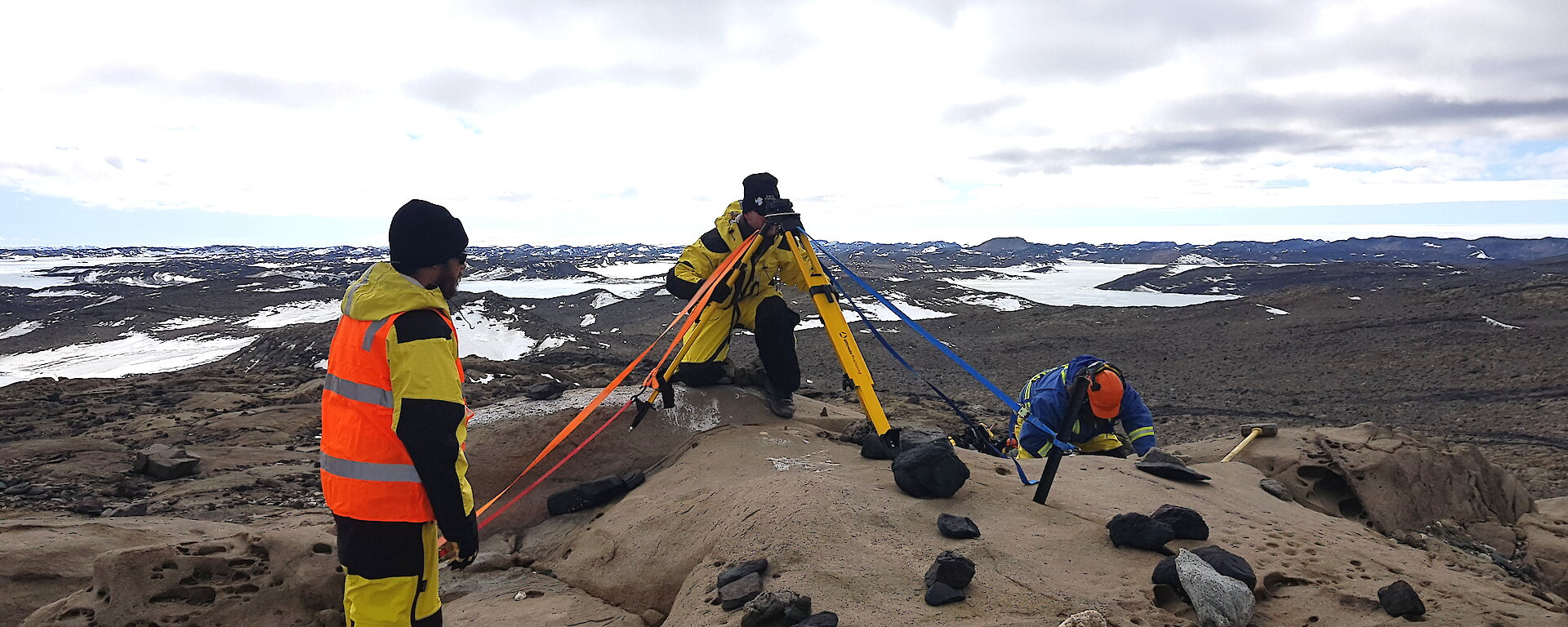 3 people with surveying equipment in a rocky landscape.
