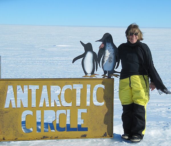 Woman stands on ice at Antarctic Circle sign.
