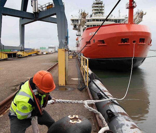 A man unties a heavy rope from the dock attached to a large ship