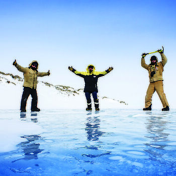 Low down camera angle of three expeditioners with raised arms standing on fresh water ice.