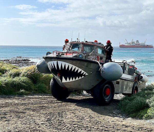 An amphibious boat on wheels with teeth painted on the front crosses the beach