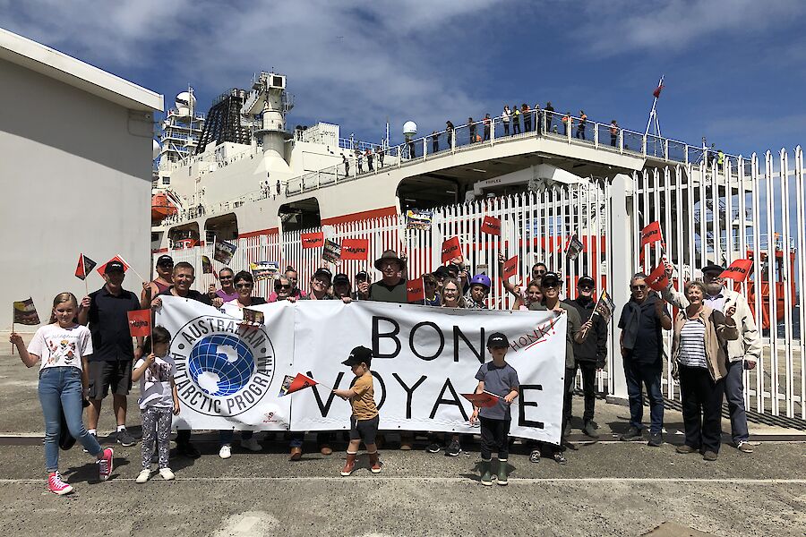 A group of people gathered in front of a ship holding a large banner reading 'Bon Voyage'
