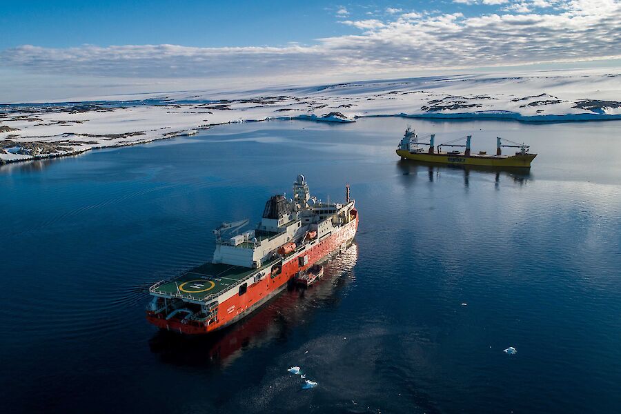 An aerial image of two ships in a natural harbour with ice on the land