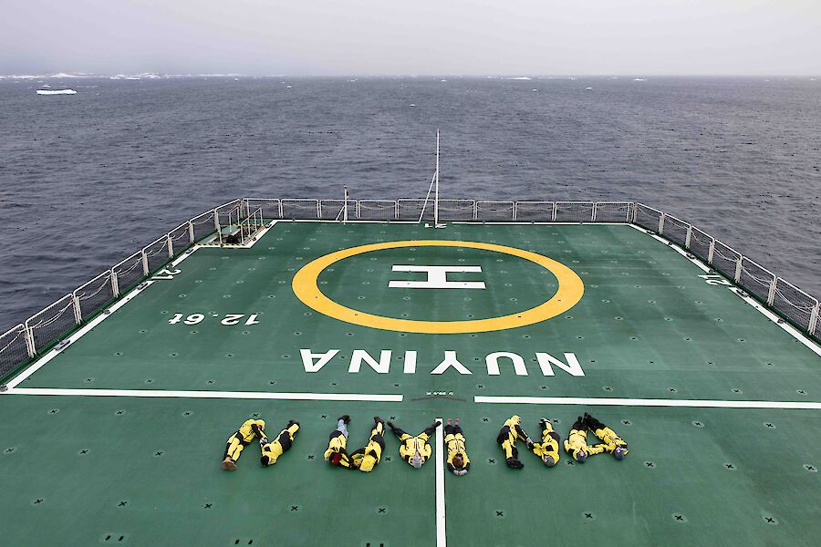 The back deck of ship with people laid out in the shape of the letters N U Y I N A