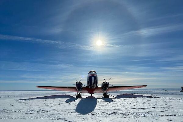Front-on view of a Basler aircraft parked on snow with a sun halo in the sky above