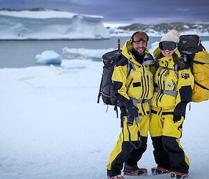 Two expeditioners pose for a photo in front of ice cliffs in the background