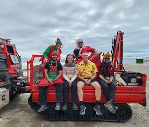 A group of expeditioners in Christmas outfits sitting on the back of an Antarctic tracked vehicle