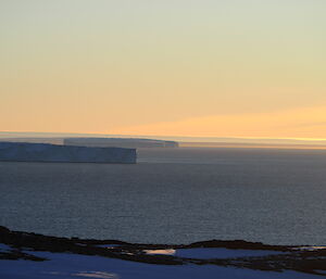 Golden glow of sunset with a still sea in the foreground and icy headlands stretching out into the bay.