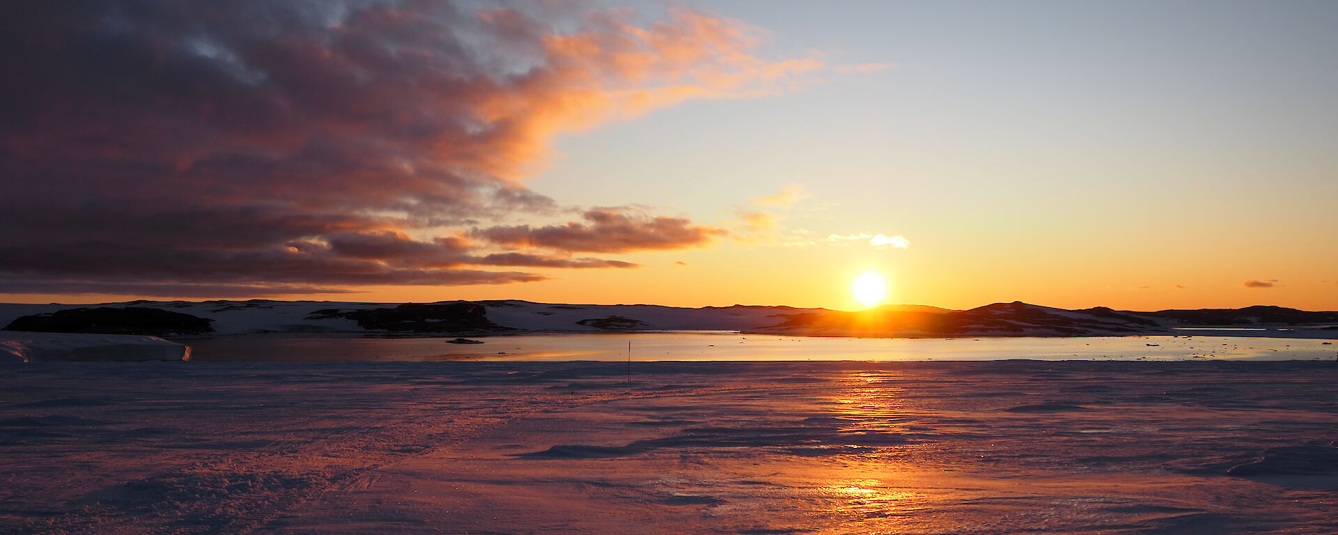The sun rises over water and ice, with pink clouds in the sky