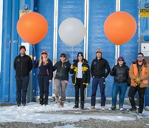 Seven expeditioners of Bureau of Meteorology pose for a photo in front of the balloon release building.