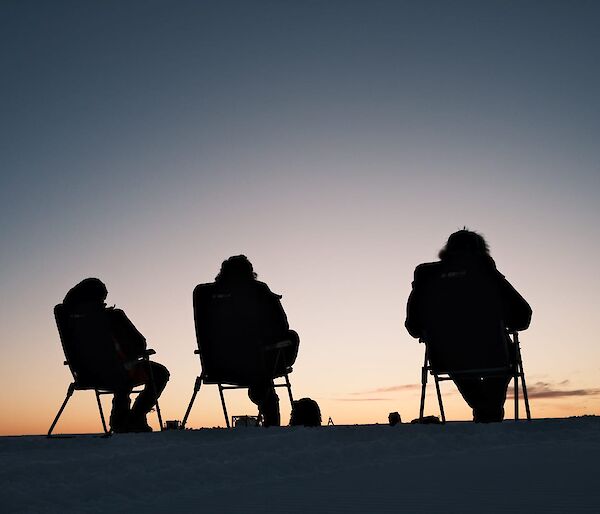 Three expeditions sitting of fold out chairs watching the sun set below the horizon