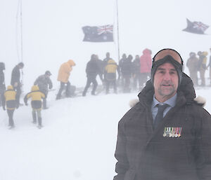 Station leader Dave Buller stands on a snowy slope with snow blowing around, with medals on his coat