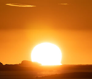 A massive yellow sun at sunset, dipping down into the sea.