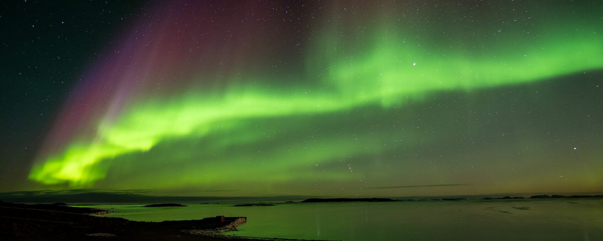 A sunning green aurora australis over the shore and bay.