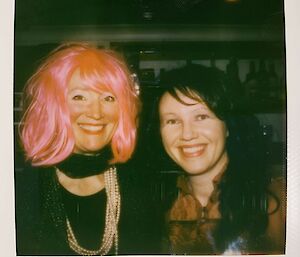 Two women wearing wigs smile at the camera