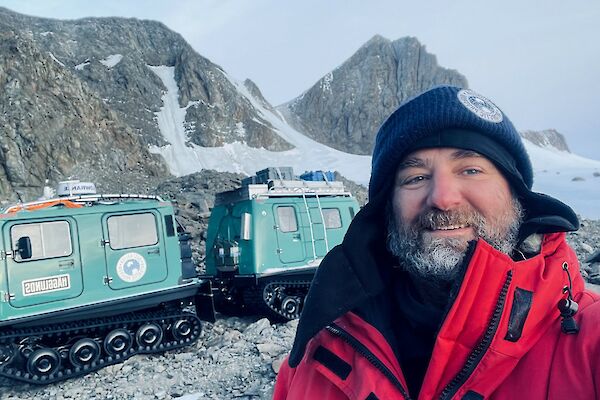 A selfie of Richard Heaton out in the Framnes Mountains near Mawson station with a green Hagglunds in the background