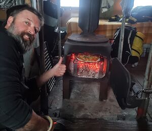 Adam smiles in front of red hot fire place at Wilkes hut