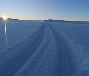 a view of fresh tracks and snow with sun setting in backround