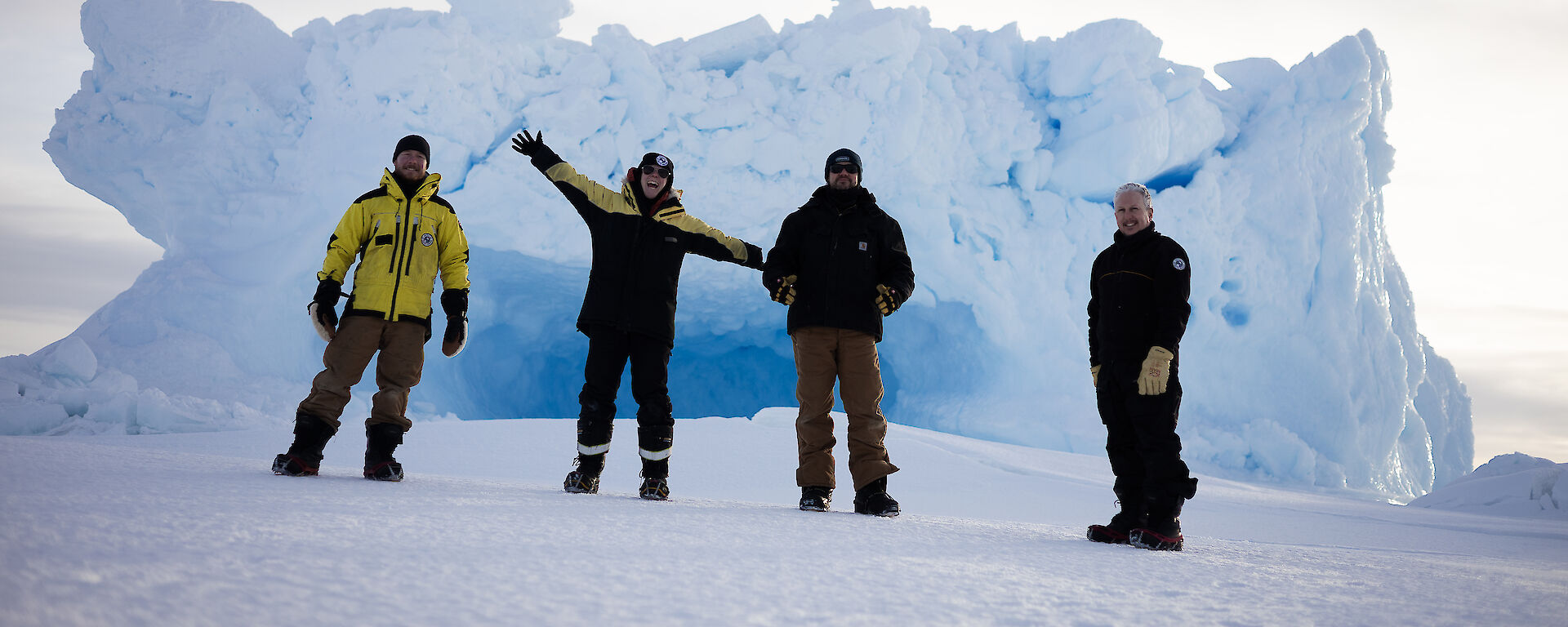 Four expeditioners in front of an iceberg.