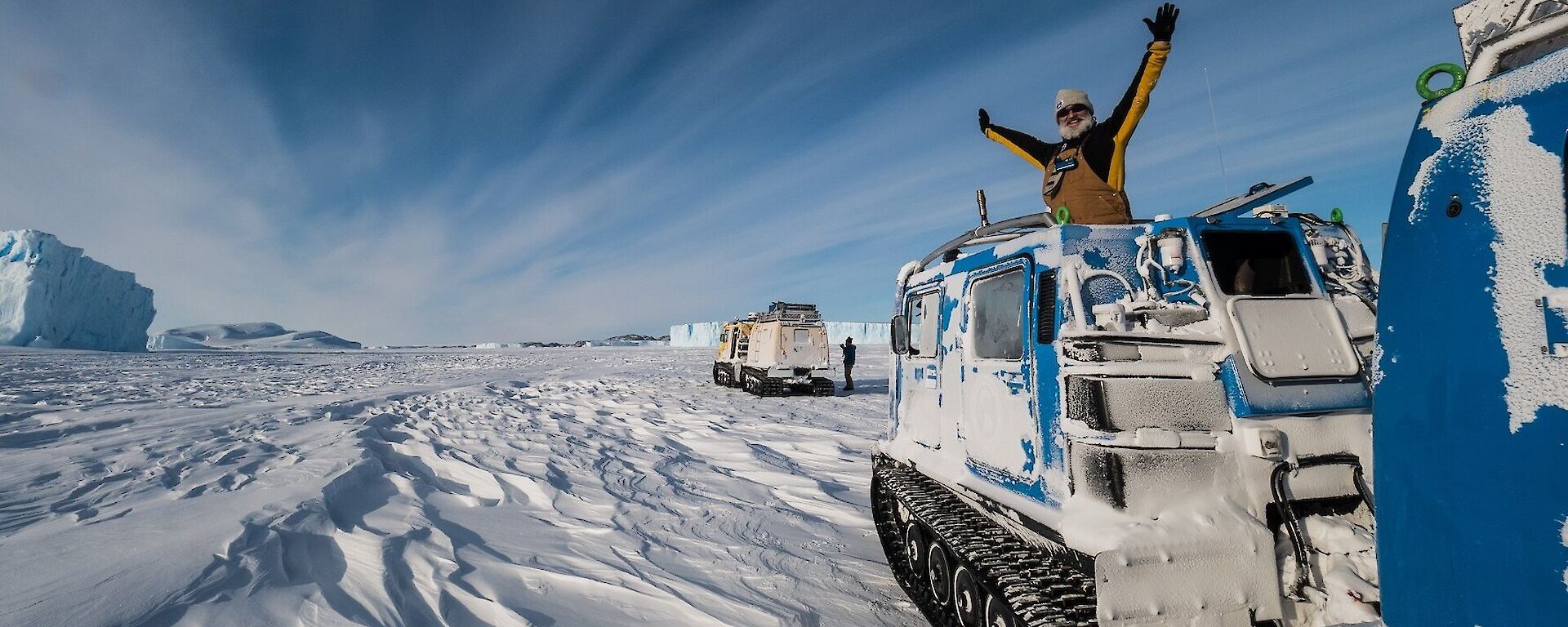 Expeditioner with arms outstretched in the roof of the oversnow vehicle parked on the ice