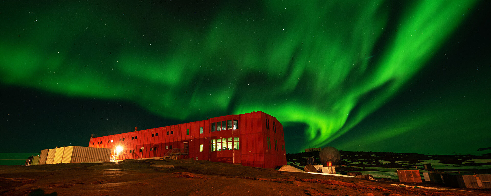 Green lights of the aurora over the red shed at Mawson station