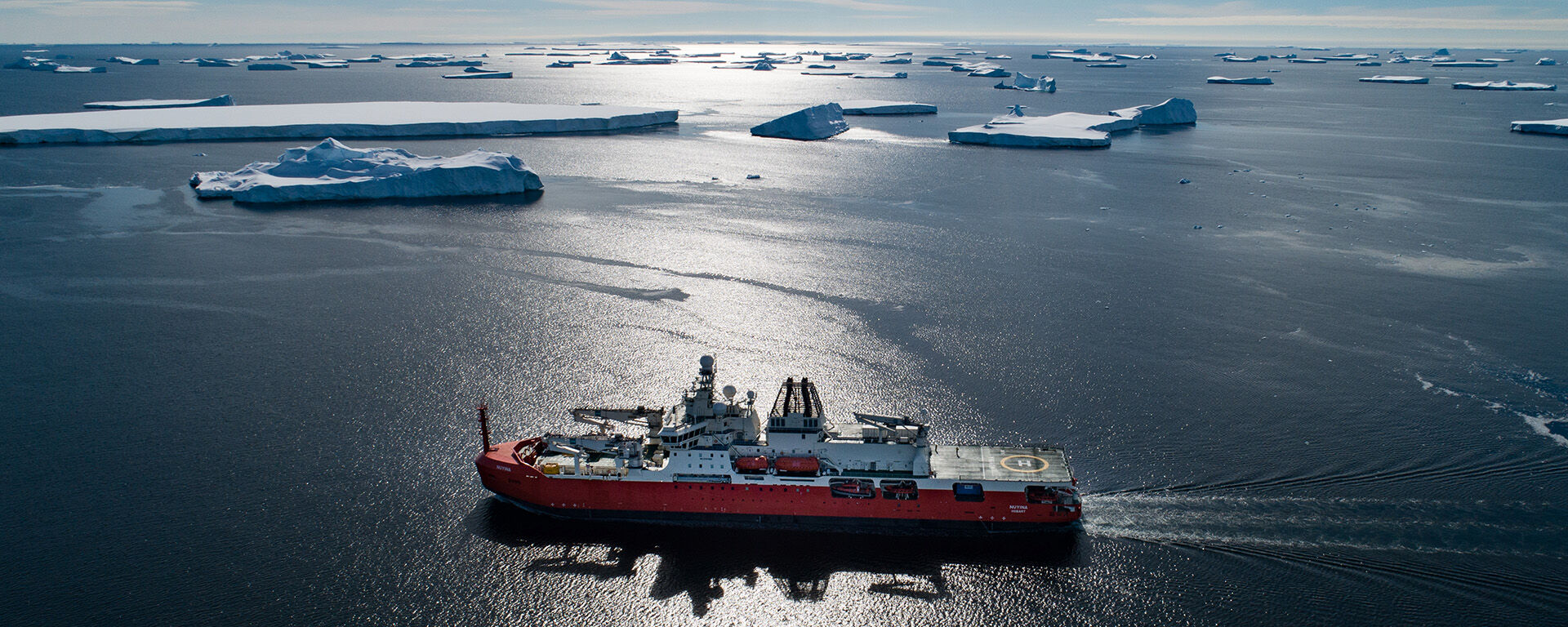 An aerial drone photo of an orange and white ship in a blue ocean with icebergs.